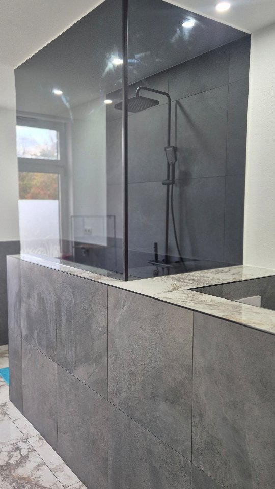 Bad mit Glas-Duschwand, großformatigen grauen Fliesen und schwarzer Regendusche
