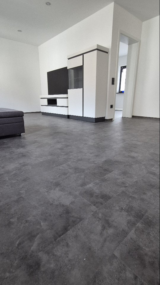 Fertiger Wohnraum mit grauem Boden in Steinoptik und weißer Wohnwand